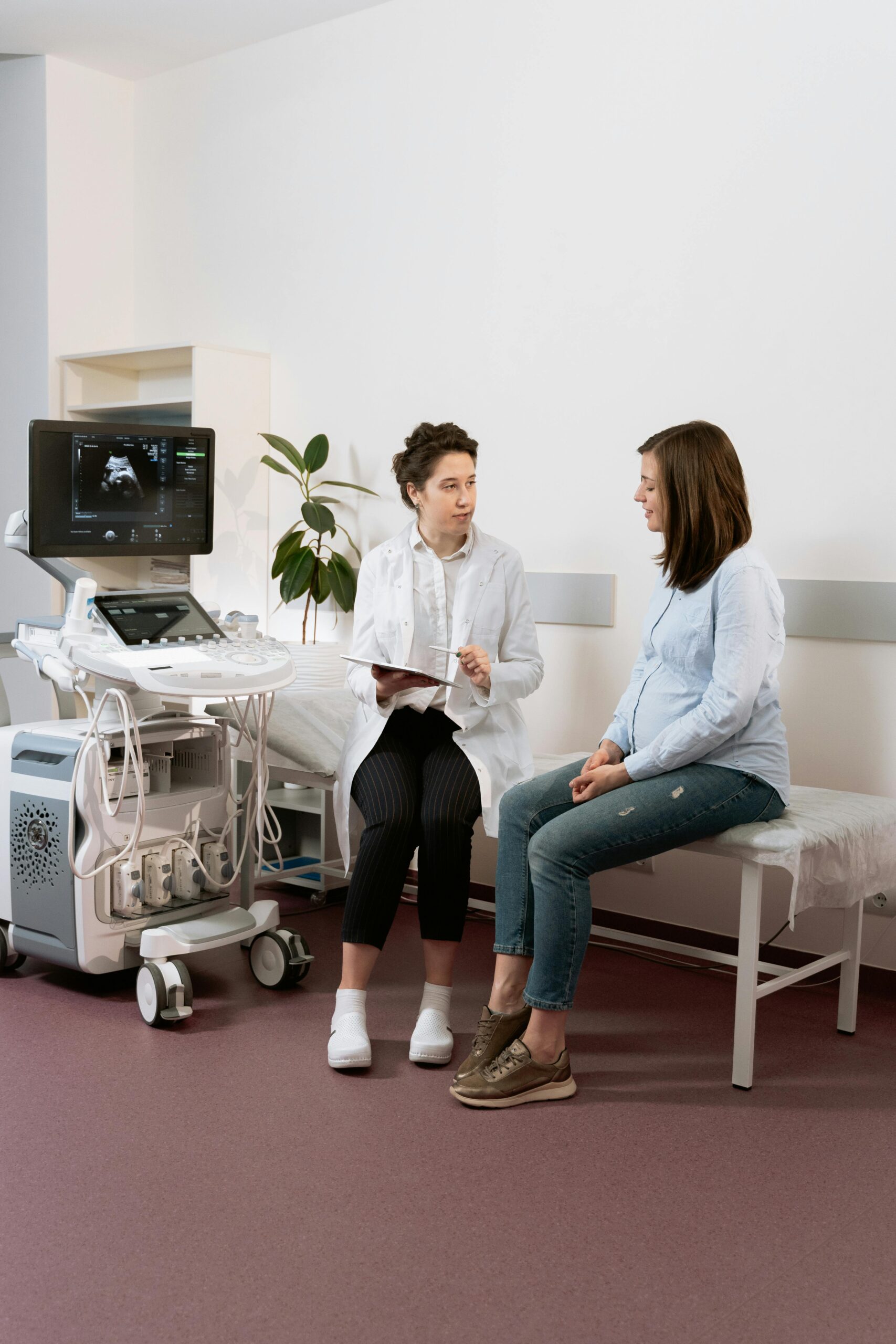 Healthcare professional consulting with a pregnant patient in a medical clinic using ultrasound equipment.